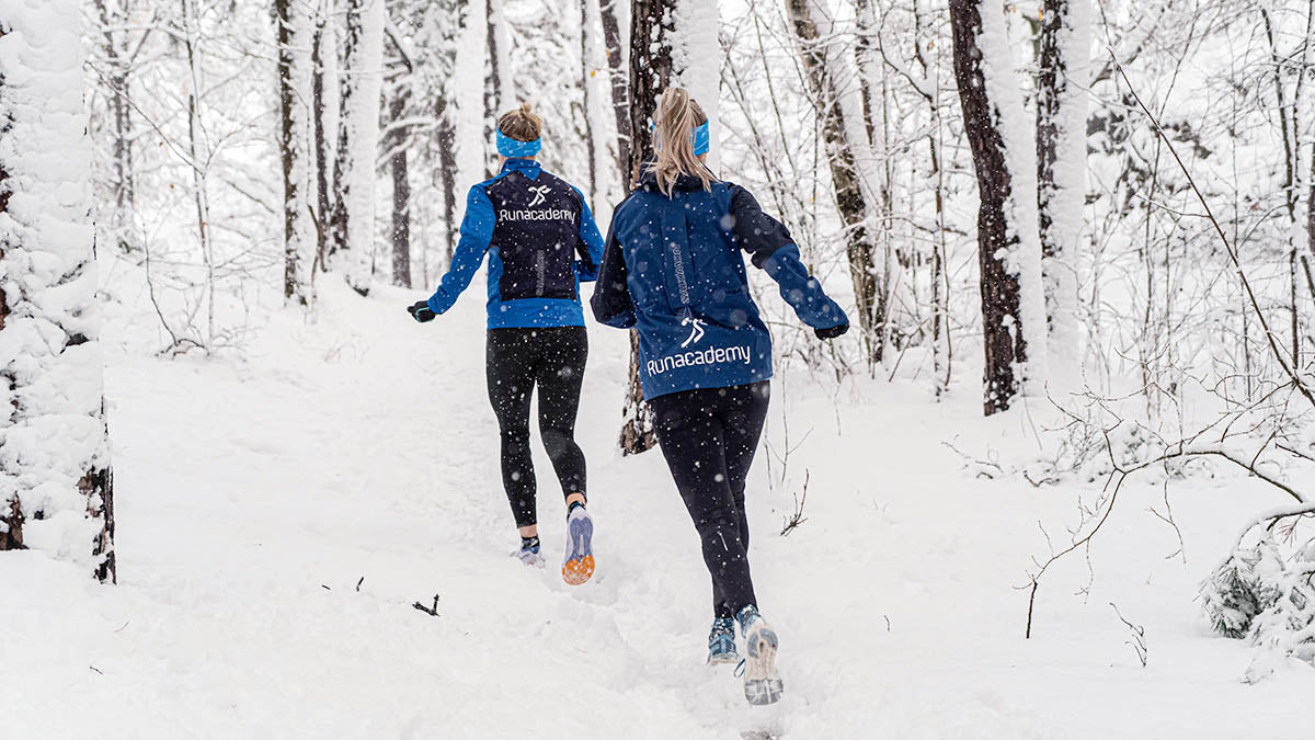 Två löpare i blå jackor som springer i snöig skog